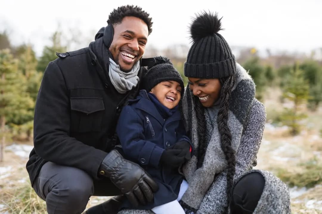A smiling family of three crouching together in warm winter clothes outdoors